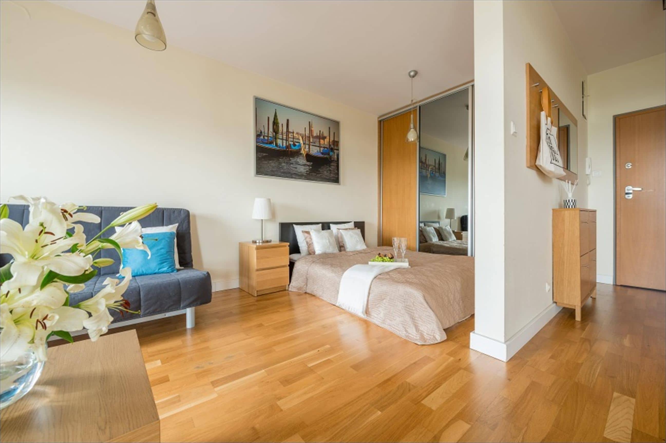 A modern bedroom with a bed, a sofa, a nightstand, a lamp, and a painting on the wall.