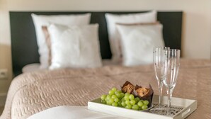 Cama bem arrumada com edredom branco e travesseiros, bandeja com uvas verdes e biscoitos de chocolate, e dois copos vazios em uma bandeja com um livro intitulado "Not to Be Repeated".