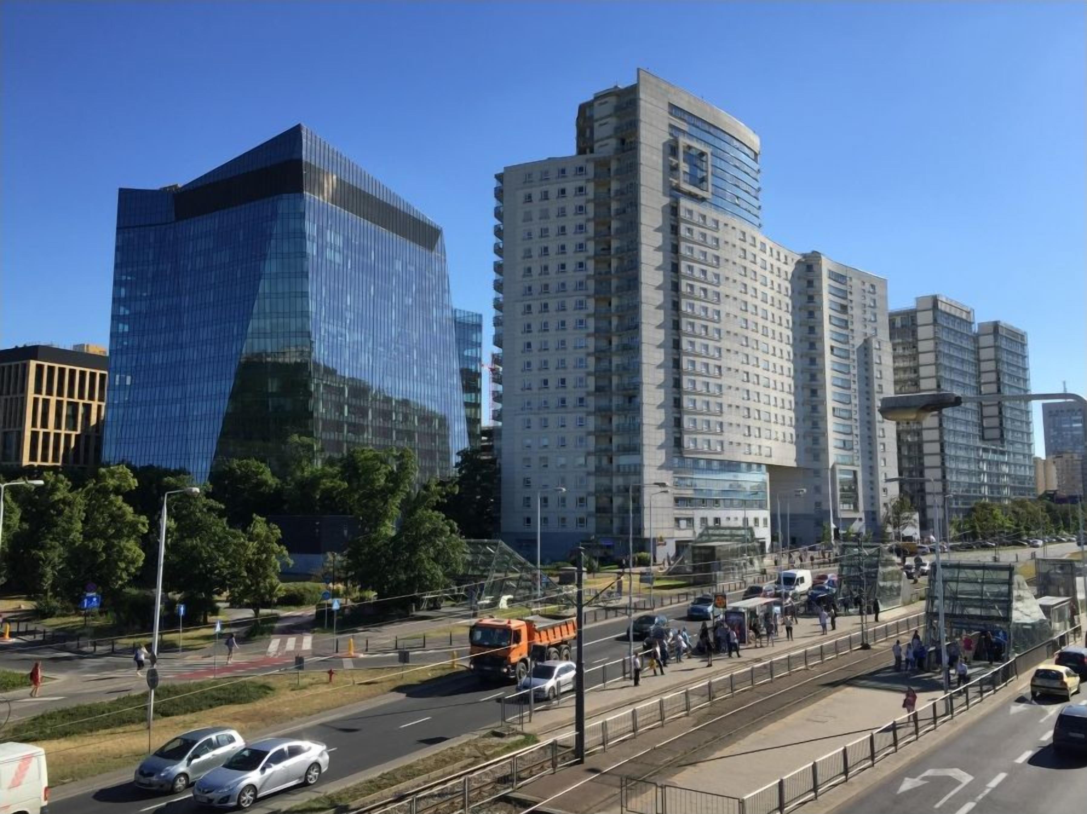 A modern urban street with high-rise buildings, a pedestrian crossing, and vehicles.
