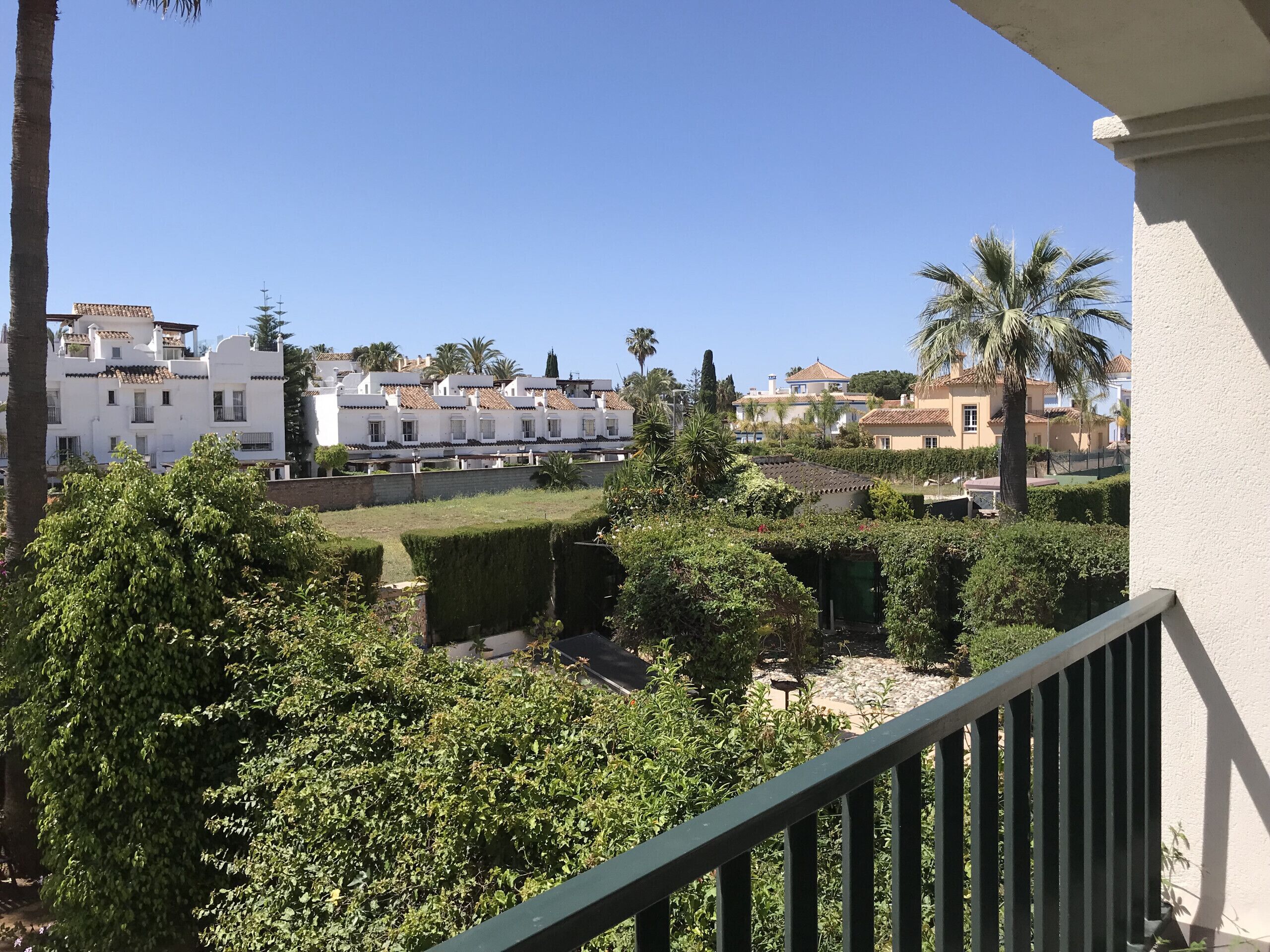 Un quartier résidentiel caractérisé par des bâtiments blancs, des palmiers et des jardins bien entretenus.