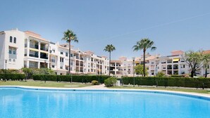 Une piscine entourée d’immeubles à plusieurs étages dotés de balcons, de palmiers et surplombant un ciel dégagé.