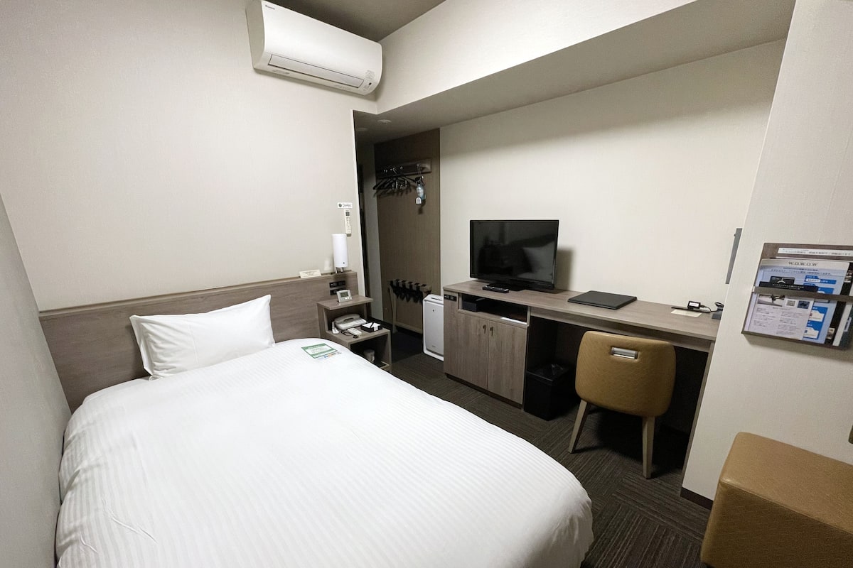 A hotel room with a bed, a desk with a computer, a television, and a chair.