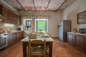 A kitchen with a tiled floor, wooden cabinets, a marble table, and a view of greenery outside.