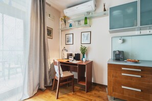 Une pièce de taille modeste, comprenant un bureau en bois, une chaise, un petit meuble et une fenêtre avec des rideaux.