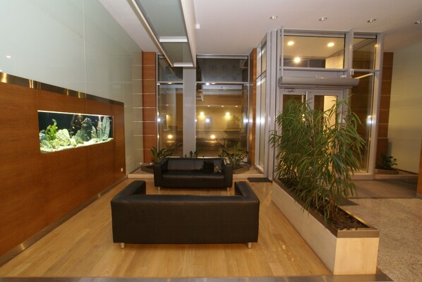 A modern lobby with a large aquarium, a black sofa, and a planter with green plants. - P&O Apartments Arkadia 2 (Warsaw)