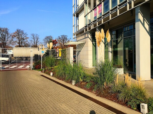 Un bâtiment moderne doté d’une entrée sécurisée par un portail, d’un chemin piétonnier dallé et d’une grande variété de plantes.
