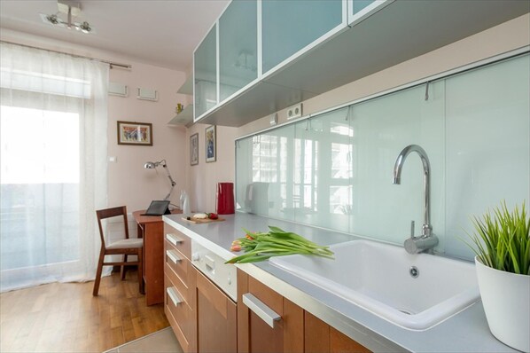A modern kitchen with a white sink, wooden cabinets, and a glass backsplash. - P&O Apartments Arkadia 2 (Warsaw)