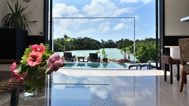 Ein modernes Zimmer mit Glastisch, Blumenvase, Blick auf Pool und See sowie Sitzgelegenheit im Freien.