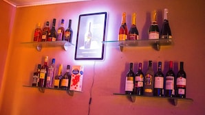 A bar area with shelves of various liquor bottles and a neon sign. - Esporta Suites - Agindingbi (Lagos)