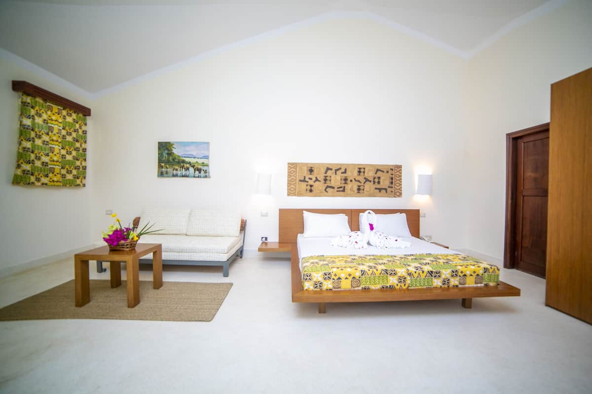 A bedroom with a bed, a sofa, a small table with flowers, and a wall with a painting.