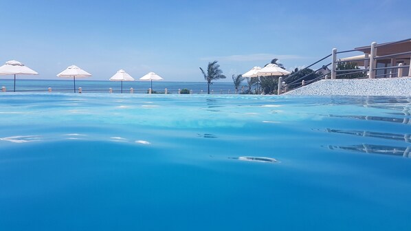 A clear blue pool with umbrellas and a view of the ocean.