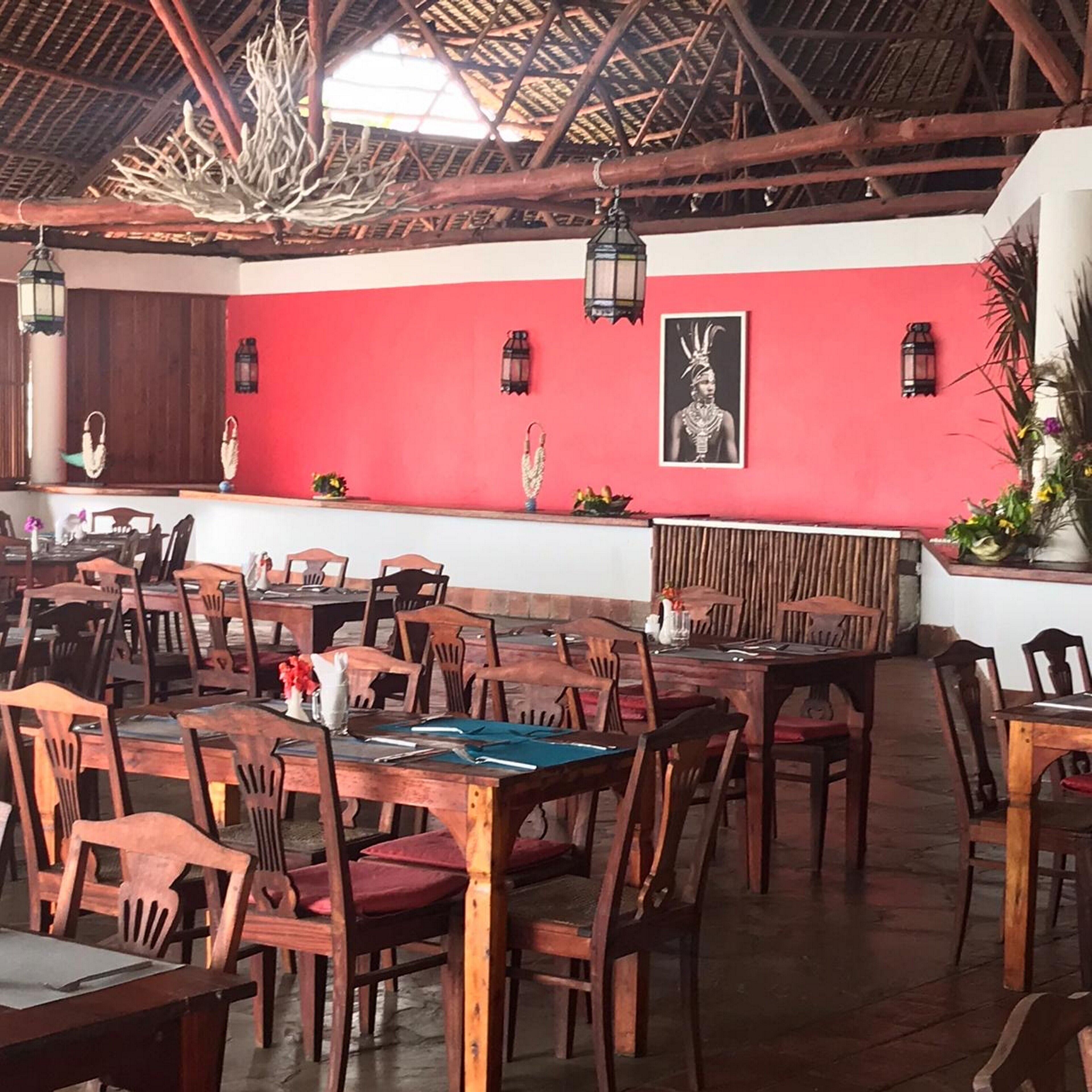 A restaurant with wooden tables and chairs, a red wall with a framed picture, and hanging lanterns.