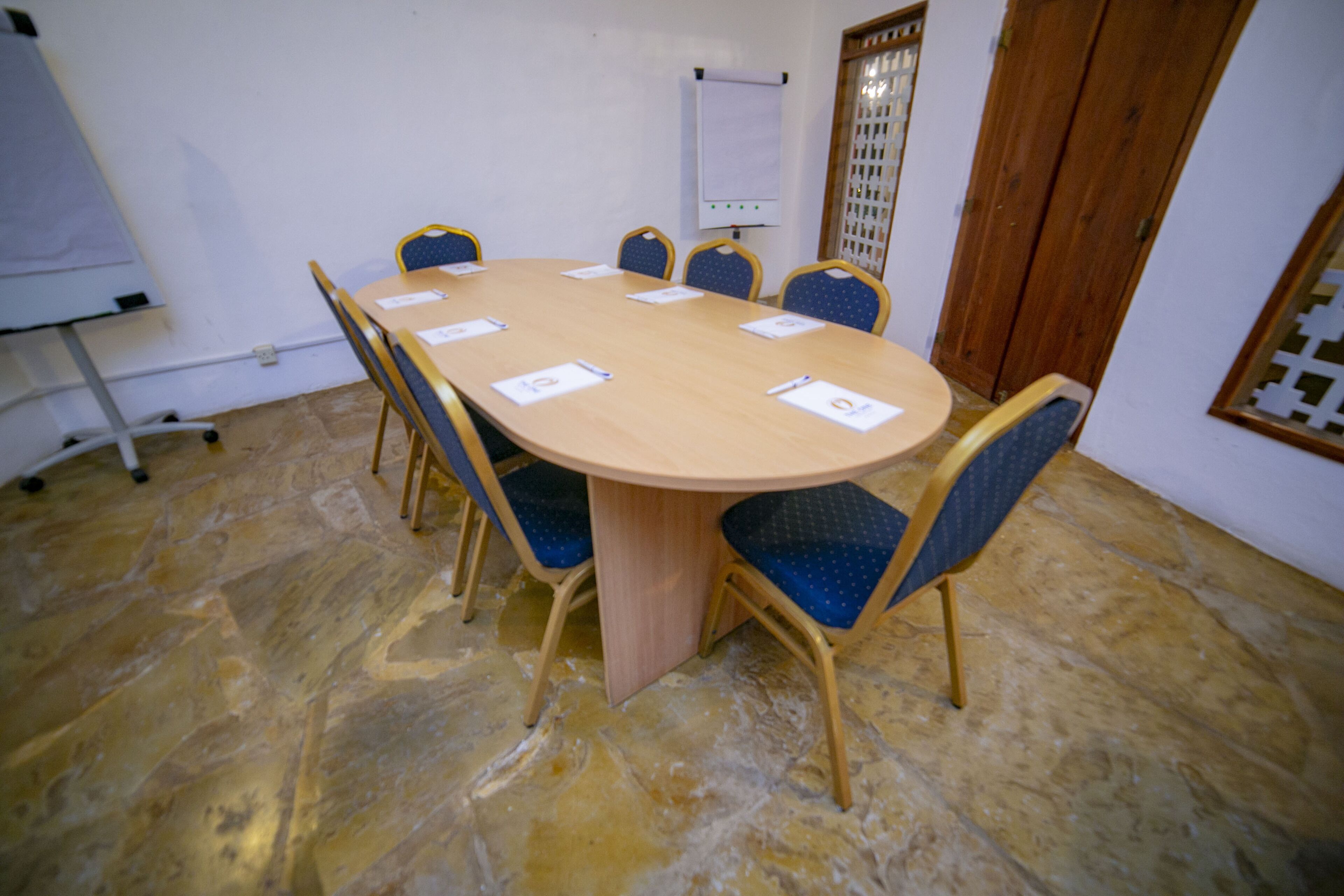A conference room with a round table, six chairs, a whiteboard, and a wooden door.