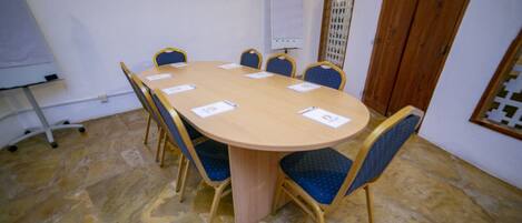 A conference room with a round table, six chairs, a whiteboard, and a wooden door.