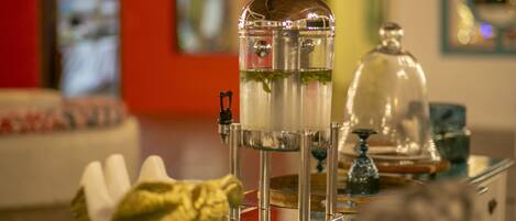 A glass coffee urn with a metal base and a dome lid, placed on a reflective surface.