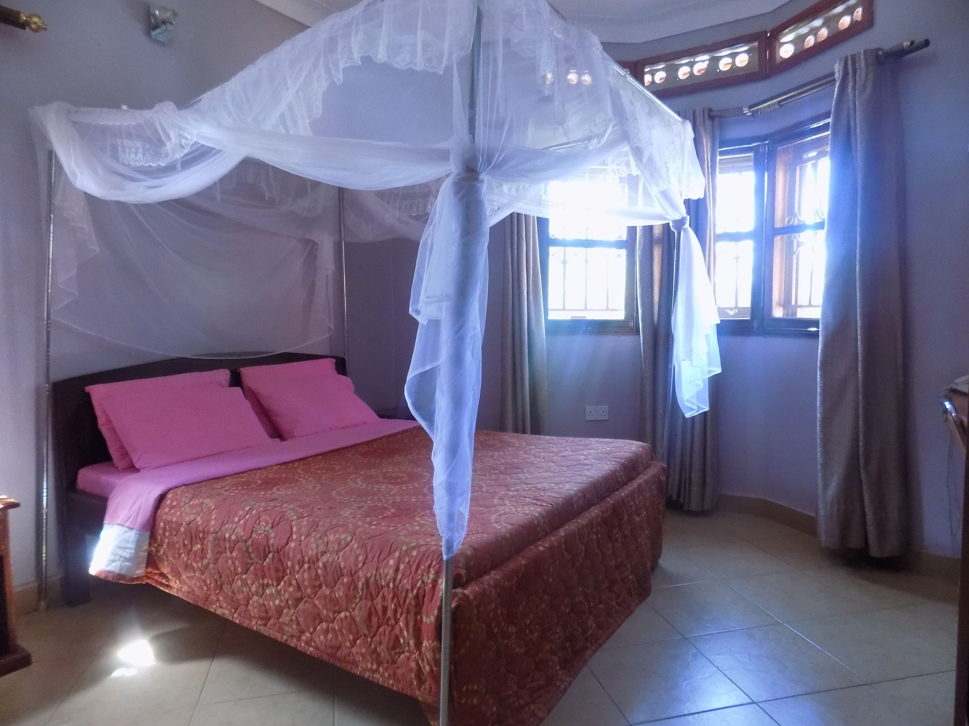 A bedroom with a bed, pink pillows, a canopy, and a window with curtains.