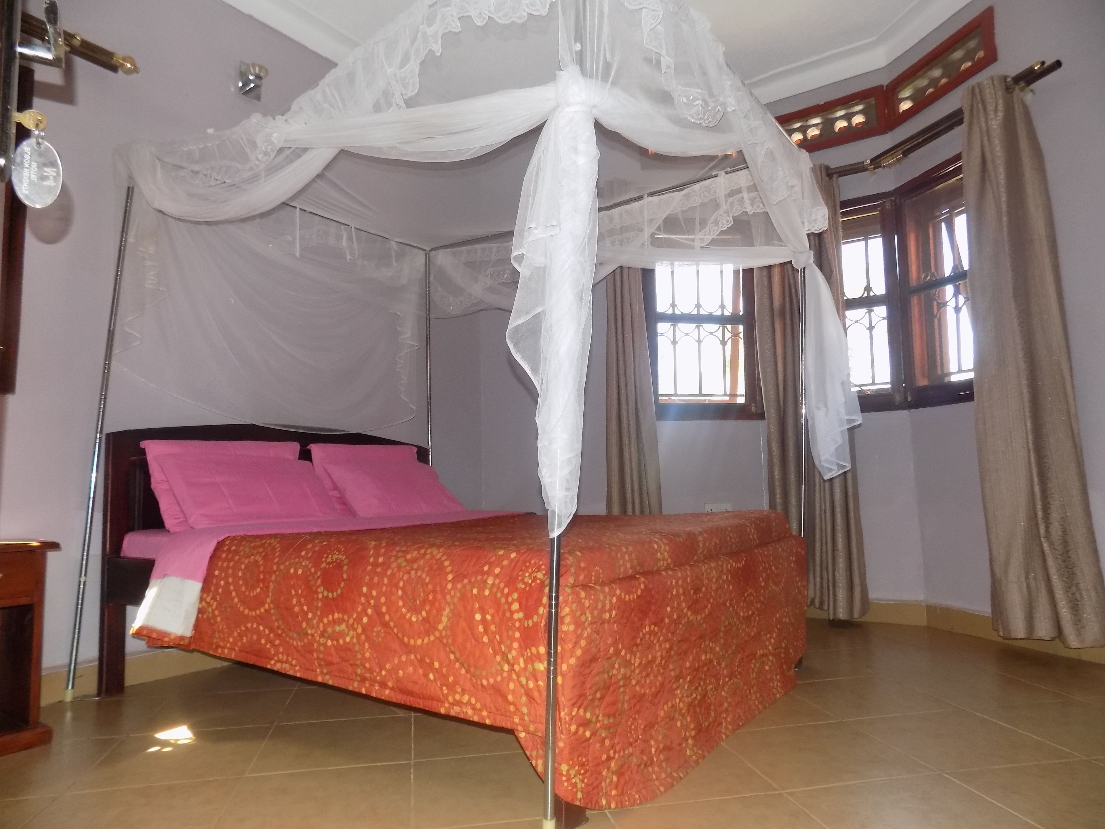 A bedroom with a bed under a canopy, a window with curtains, and a tiled floor.