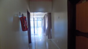 Un couloir avec un extincteur sur le côté gauche, une porte sur le côté droit et un hall lumineux au bout.
