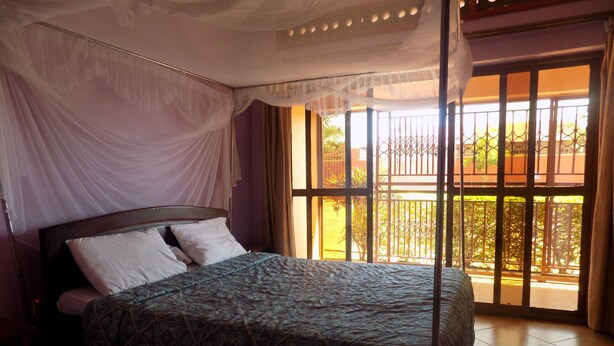 Une chambre à coucher avec un lit, un baldaquin et une vue sur l’extérieur par une fenêtre ornée d’une grille en métal.
