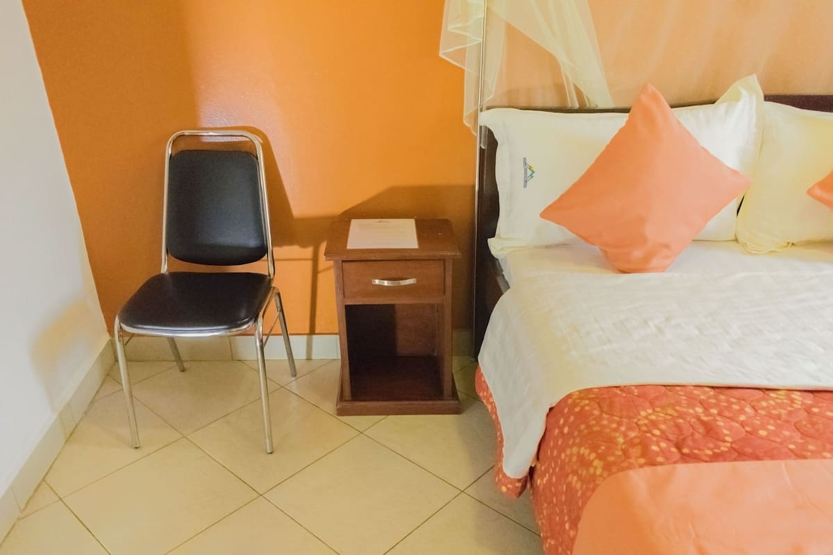 A room with a bed, a chair, a nightstand, and a window with a curtain.