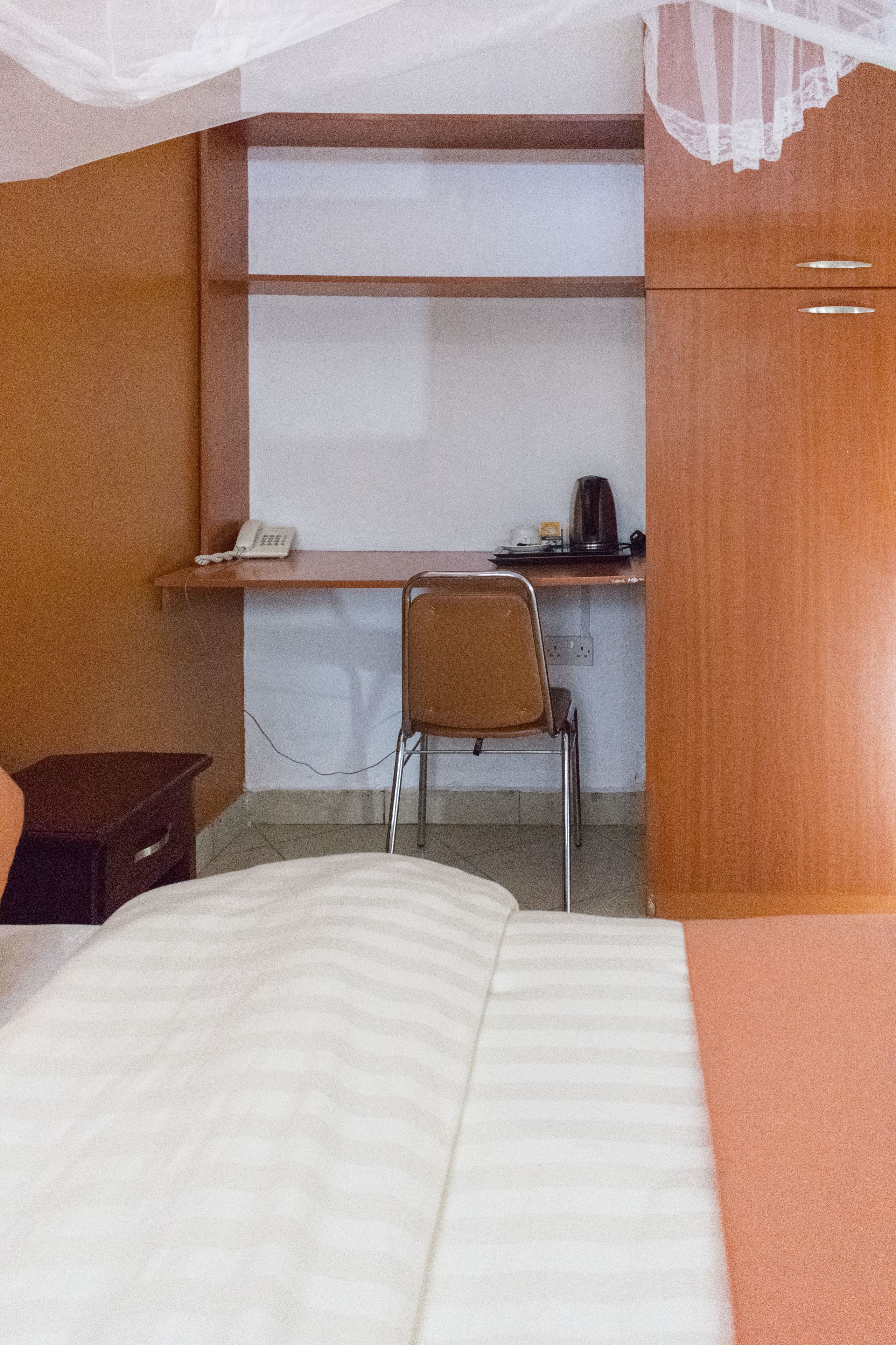 A bedroom with a bed, a desk with a chair, a telephone, and a coffee maker.