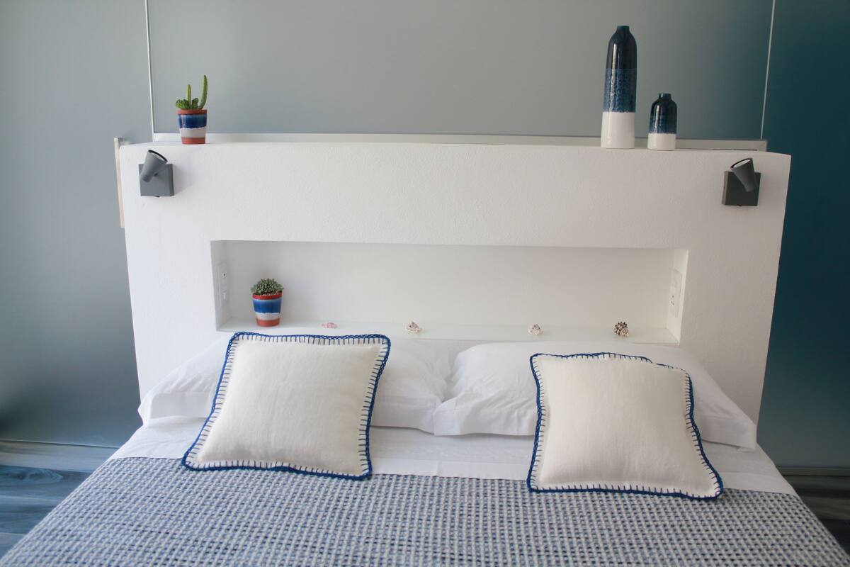 A bed with white bedding and blue trim, a small potted plant, and a water bottle on the headboard.