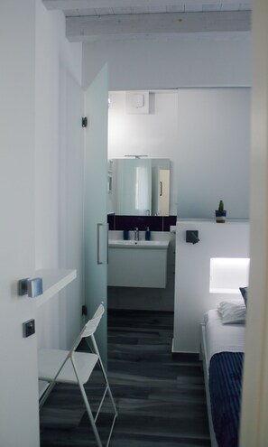 Une chambre d’hôtel moderne avec salle de bain, un lit et une petite plante en pot.