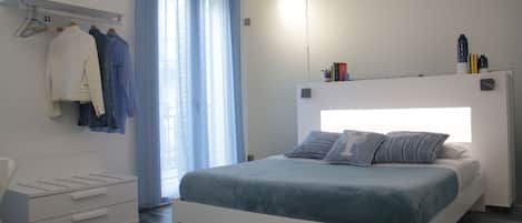 Un dormitorio moderno con cama, mesitas de noche, un armario y una ventana con cortinas.