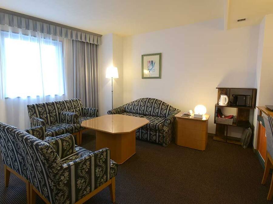Habitació d'hotel amb dos sofàs estampats, una taula de centre de fusta, una taula auxiliar amb una làmpada, una televisió i un microones.
