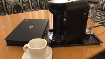 A coffee maker on a table with a cup and saucer, a box labeled 'DRIP POD', and a glass measuring cup.