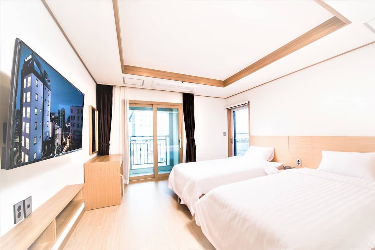 A hotel room with two beds, a large window, a balcony, and a cityscape view.