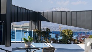 A modern building with a glass facade, a mountain view, and outdoor seating with potted plants. - Run Hotel (Seogwipo)