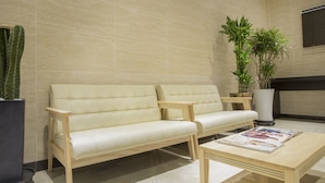 A modern waiting area with a beige sofa, a wooden coffee table, and a potted plant. - Run Hotel (Seogwipo)