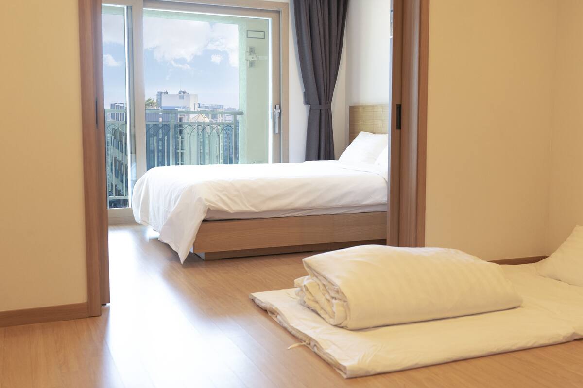 A hotel room with a bed, a chair, and a view of the cityscape through a large window.