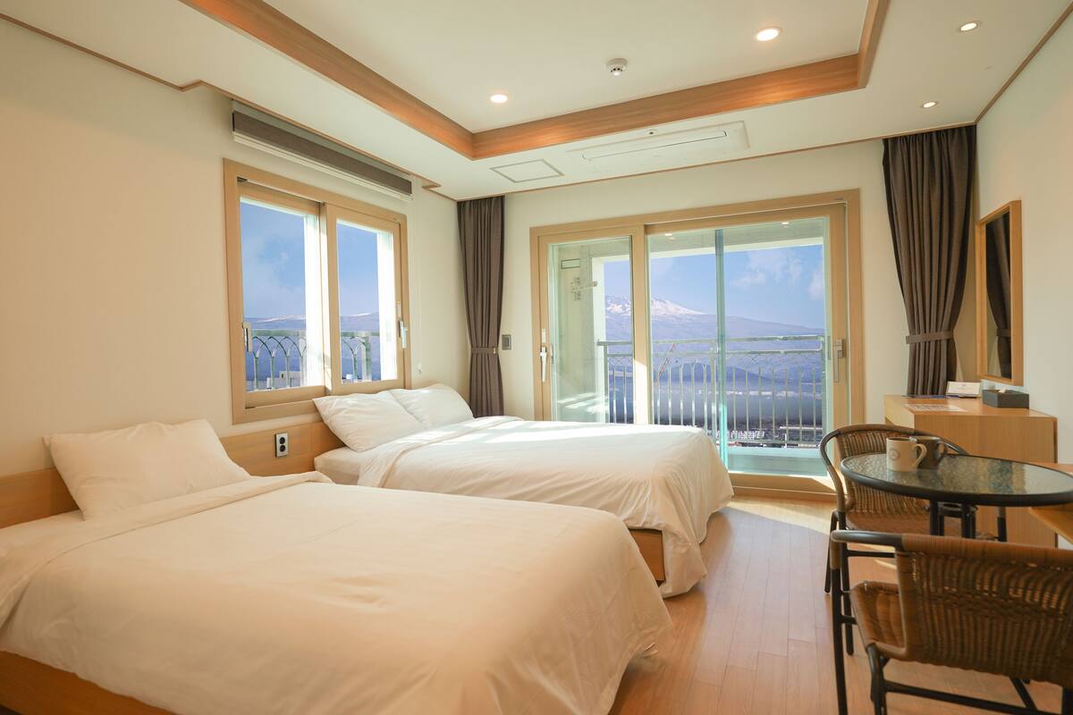 A hotel room with two beds, a balcony with a view, a small table with a chair, and a desk with a chair.