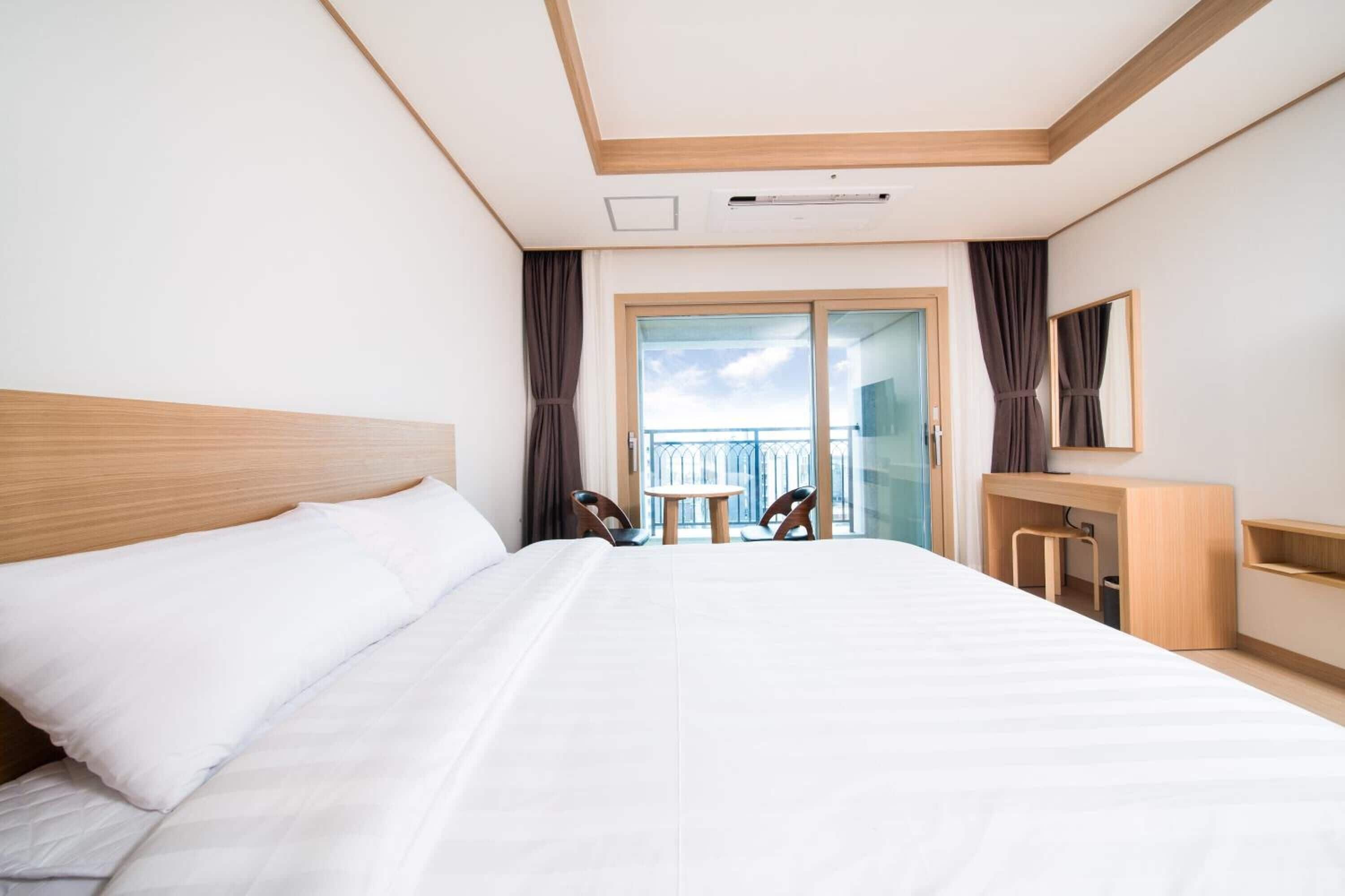A hotel room with a large bed, a desk, a chair, a small table, and a balcony with a view.