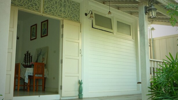 A white building with a porch, a closed garage door, and a staircase leading up to the entrance. - Villa Sittiprapa (Nakhon Ratchasima)