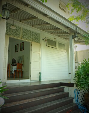A white building with a porch, a closed garage door, and a staircase leading up to the entrance.