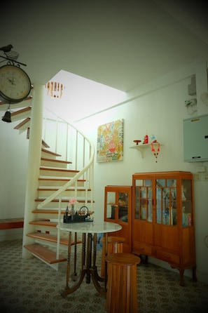 A room with a spiral staircase, a wooden cabinet with glass doors, a small round table, and a wall clock.