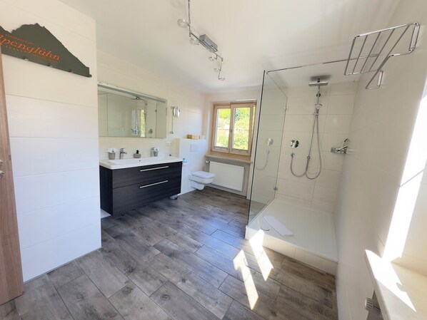 A modern bathroom with a large mirror, a vanity with a dark cabinet, a toilet, and a glass-enclosed shower area.