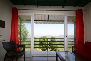 Een kamer met een schuifglazen deur die uitkomt op een balkon met uitzicht op bomen en heuvels.