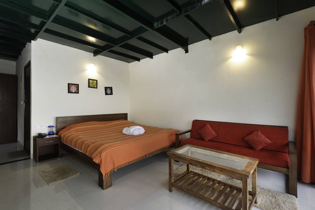 A bedroom with a bed, a red sofa, a wooden coffee table, and a nightstand.