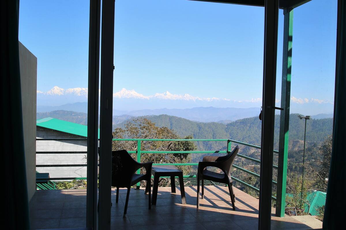 A balcony with a table and two chairs, overlooking a mountainous landscape with snow-capped peaks.