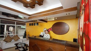 Een hotel receptie met een houten receptiebalie, een bord met de uiterlijke tijd, een kerstboom en een grote ronde wanddecoratie.