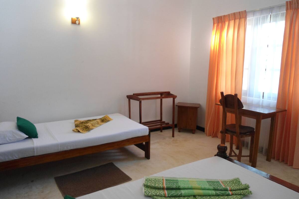 Quarto com duas camas de solteiro, uma escrivaninha, uma cadeira e uma mesinha.