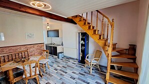 A spacious living area with a wooden staircase, a dining table with chairs, and a kitchen in the background. - Apartment 01 (right) - Holiday apartments Groth family (Heringsdorf)