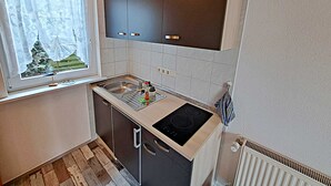 A compact kitchen with dark cabinets, a sink, and a stove. - Apartment 01 (right) - Holiday apartments Groth family (Heringsdorf)