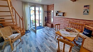 A cozy room with a wooden staircase, a dining area with a table and chairs, and a view through a glass door to an outdoor area. - Apartment 01 (right) - Holiday apartments Groth family (Heringsdorf)