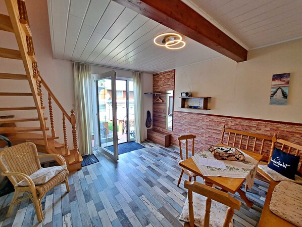 A cozy room with a wooden staircase, a dining area with a table and chairs, and a view through a glass door to an outdoor area.