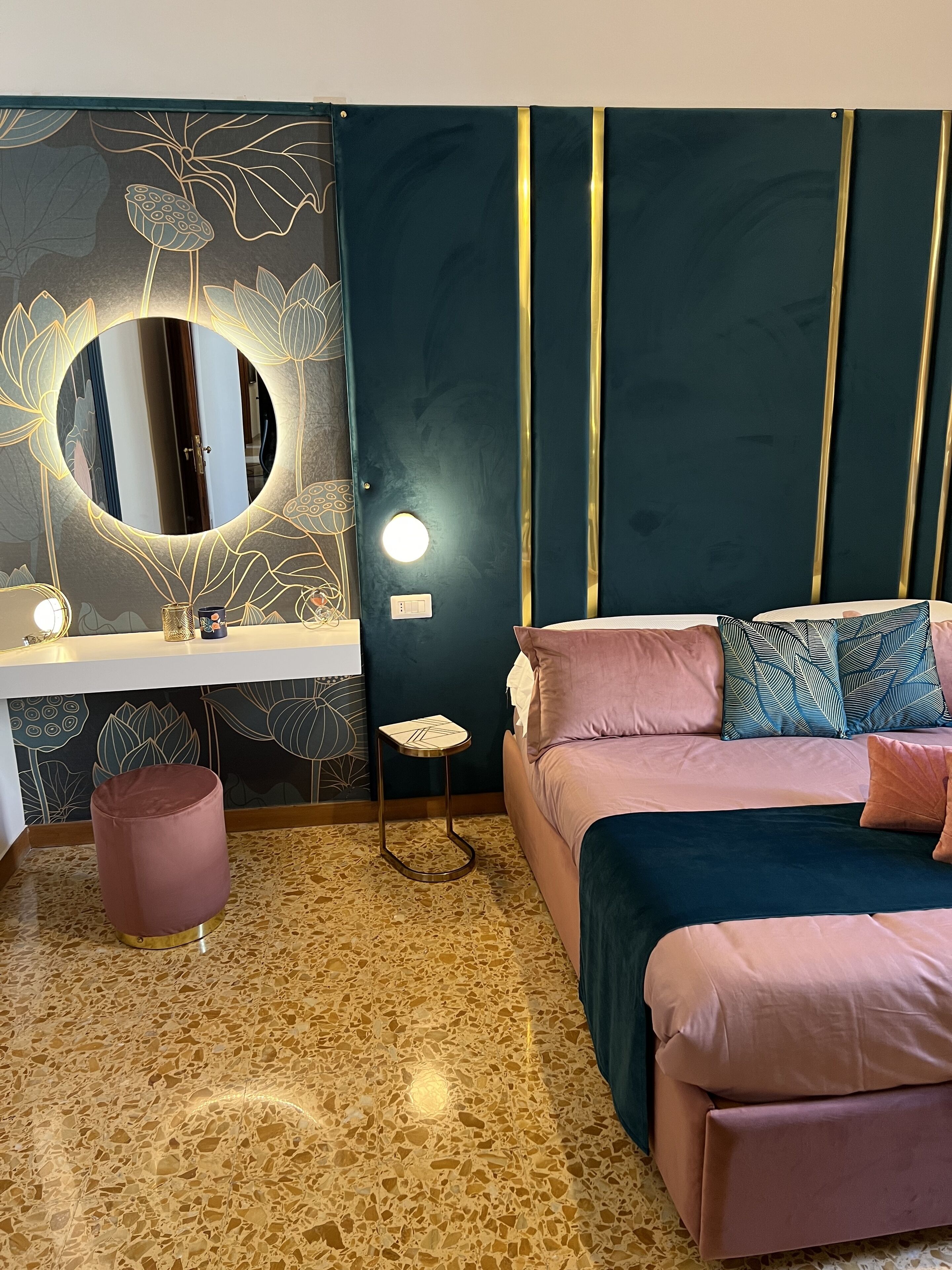 A bedroom with a bed, bedside table, mirror, and a small stool.